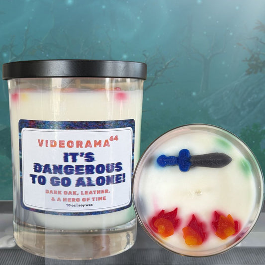 Videorama64 "It's Dangerous to Go Alone" candle with lid removed showing embedded sword and red flame wax embeds, Zelda pop culture soy candle